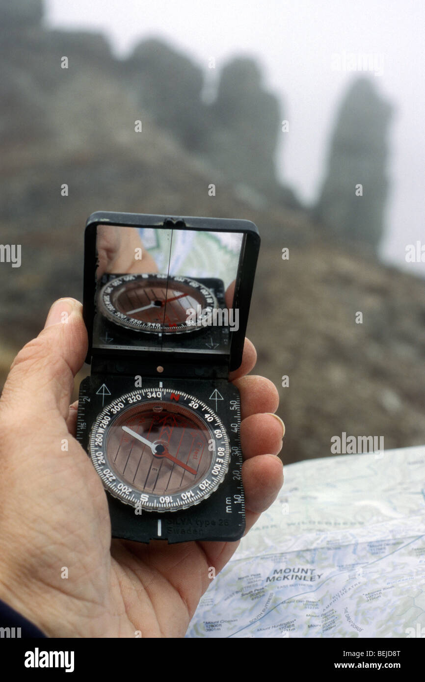 Hiker reads compass and topographic map for orientation in the fog in the mountains Stock Photo