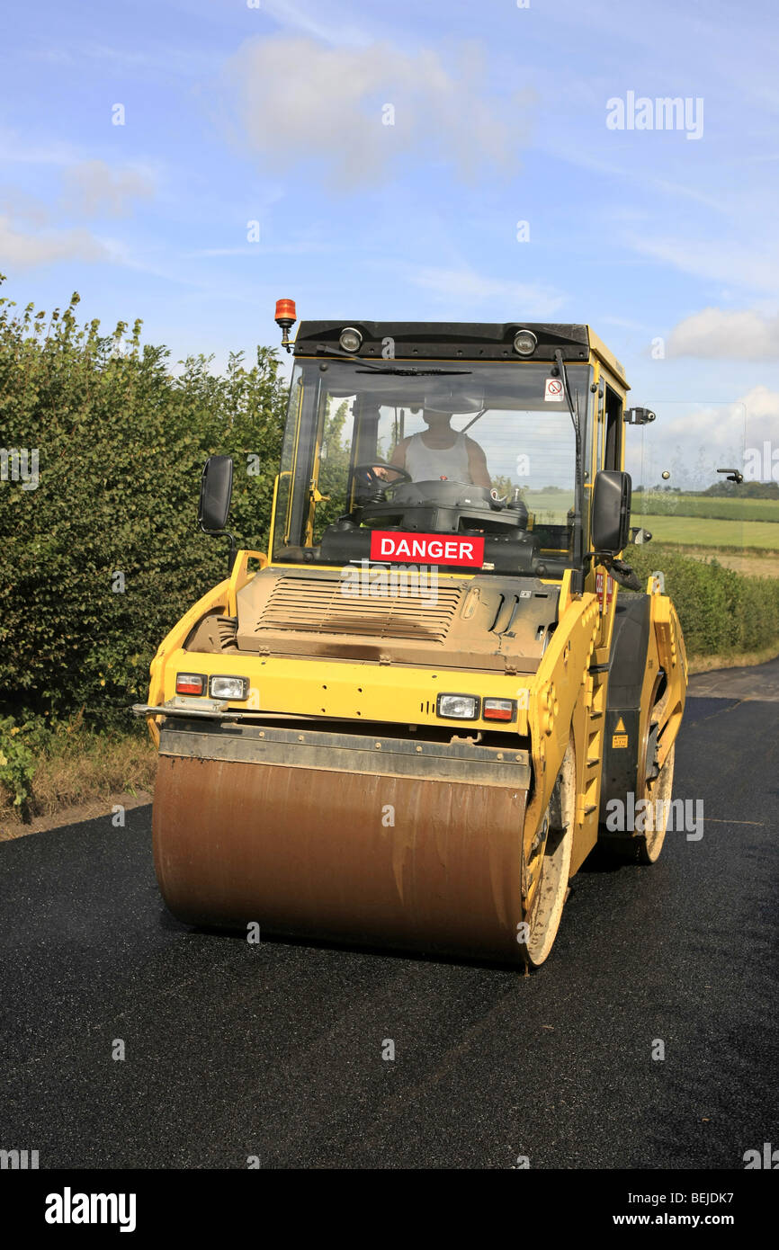 Yellow road roller at work flattening a newly laid tarmac road Stock Photo
