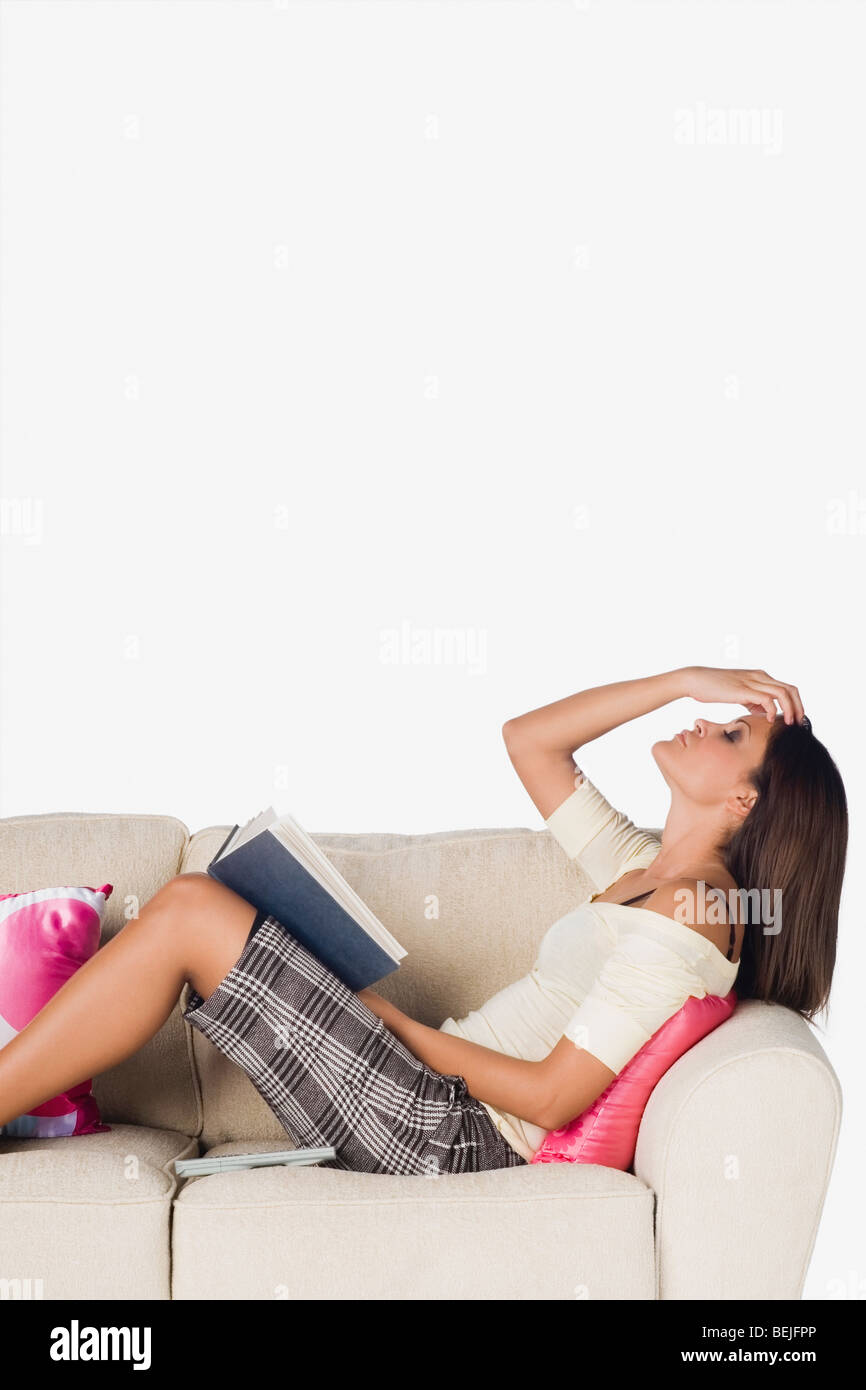 Side profile of a young woman reclining on a couch and holding a book ...