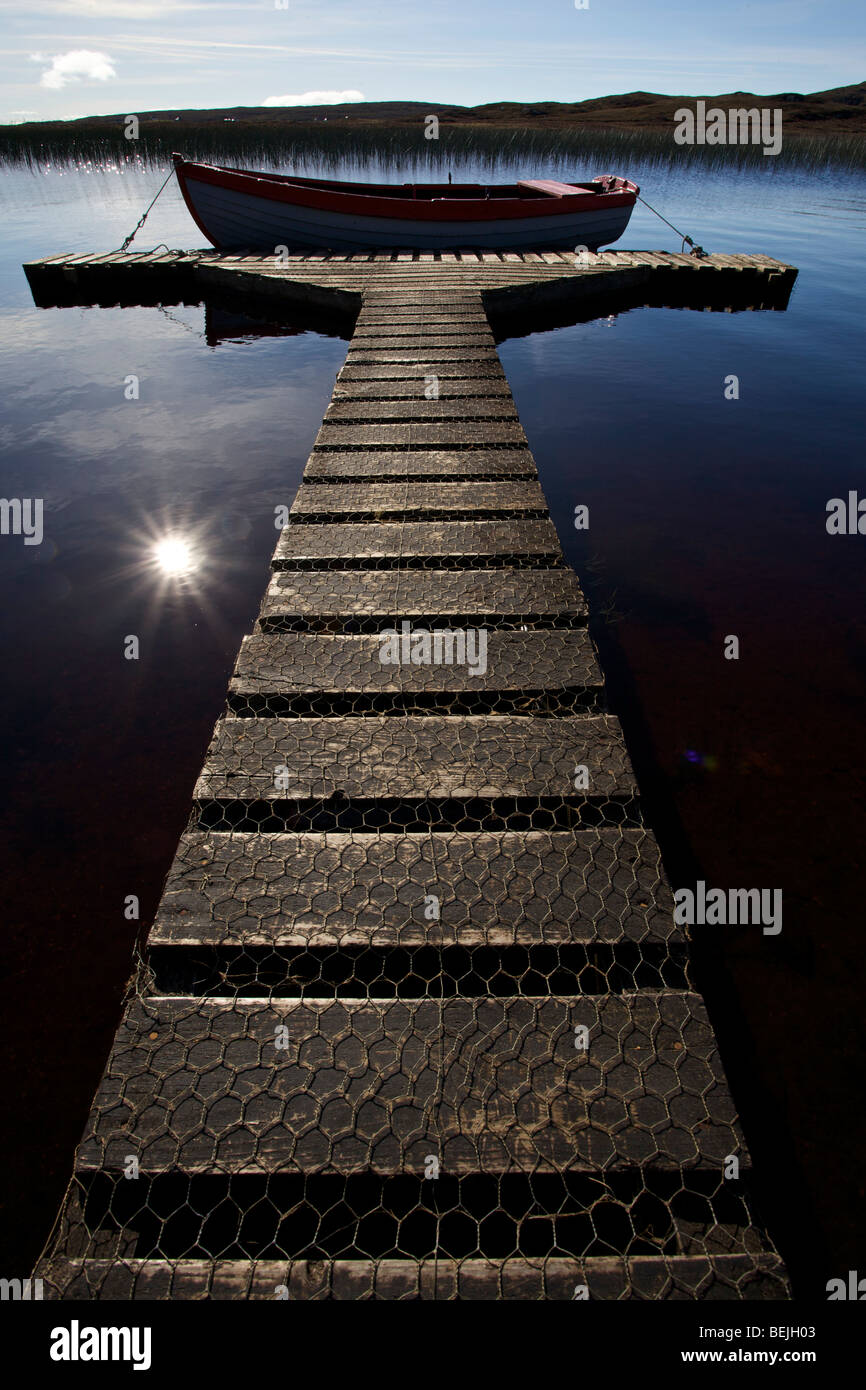 A rowing boat moored in the sunshine at the end of a wooden jetty on ...