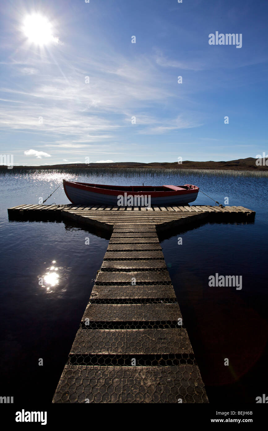 A rowing boat moored in the sunshine at the end of a wooden jetty on ...