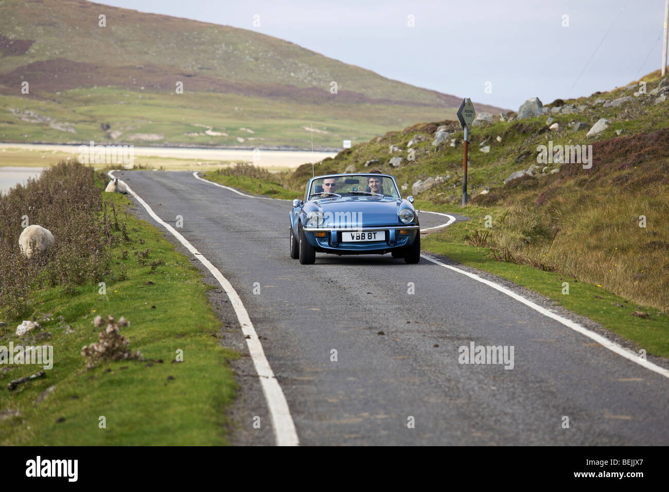 A classic sports car drives along an empty road on the Isle of Harris, Scotland Stock Photo