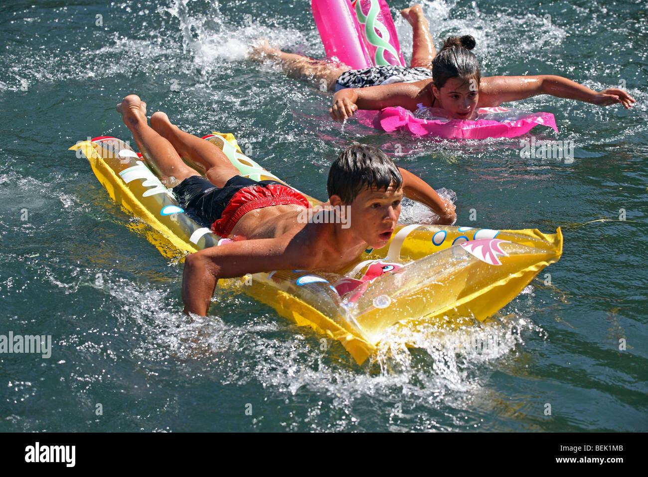 A girl and a boy swimrace with inflatable beach mattresses. Pliva