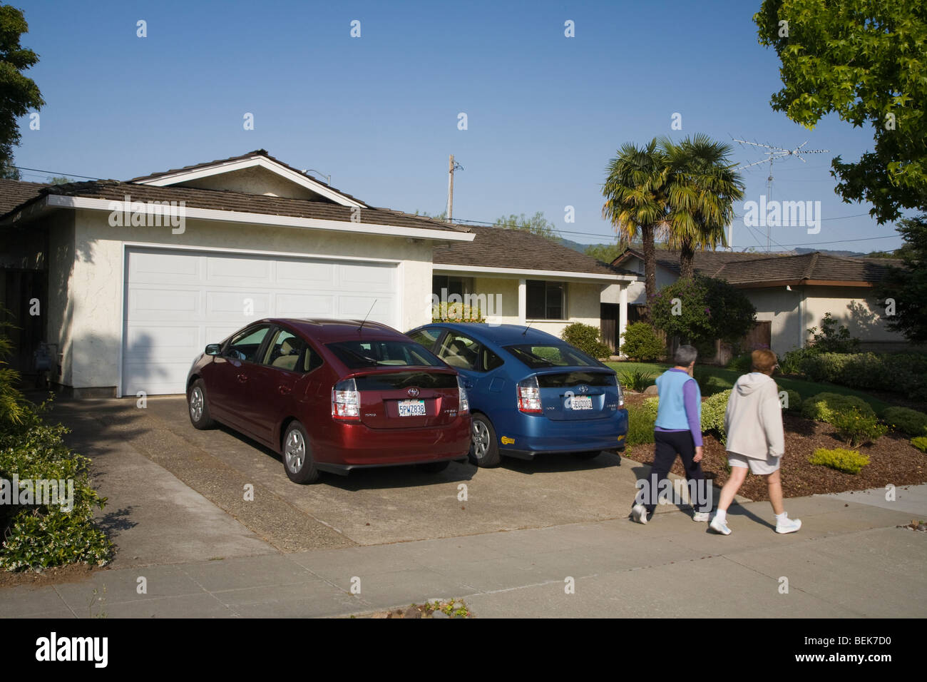 Two people passing two Toyota Prius hybrid cars which are parked in driveway. Cupertino, California, USA Stock Photo