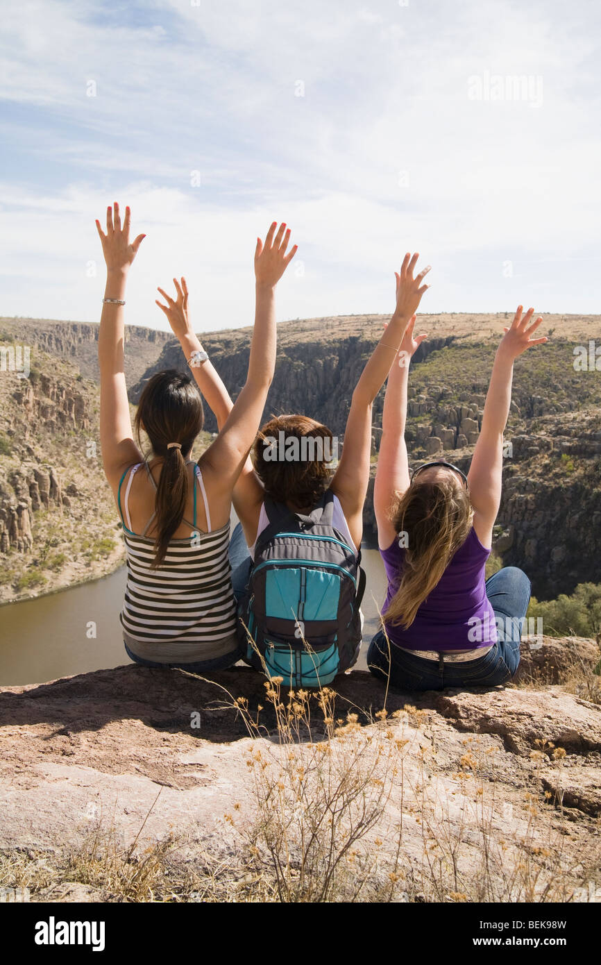Three women sitting on a mountain with their arms raised, San Jose de Gracia, Aguascalientes, Mexico Stock Photo