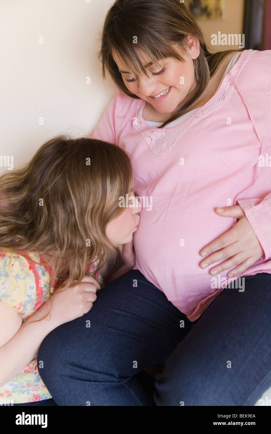 Woman kissing her pregnant sister's belly Stock Photo