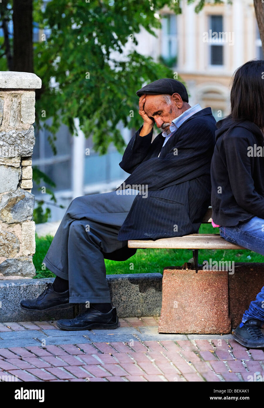 Old man sleeping outside on a bench in a city square. Stock Photo