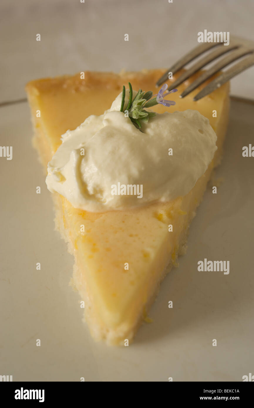 A slice of homemade lemon tart decorated with whipped cream and a rosemary flower on a white plate. Stock Photo