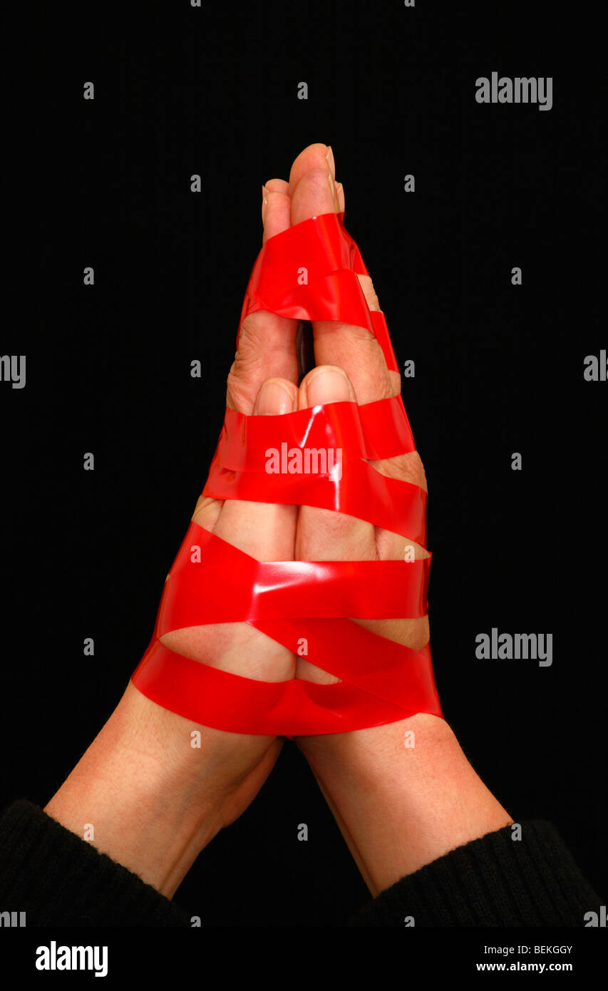 Hands bound together by red tape on a black background. Stock Photo