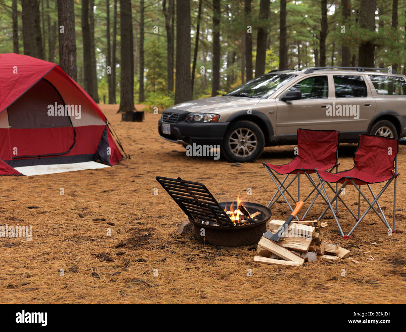 Tent, car and a burning fire with two empty chairs near it at a camping site Stock Photo