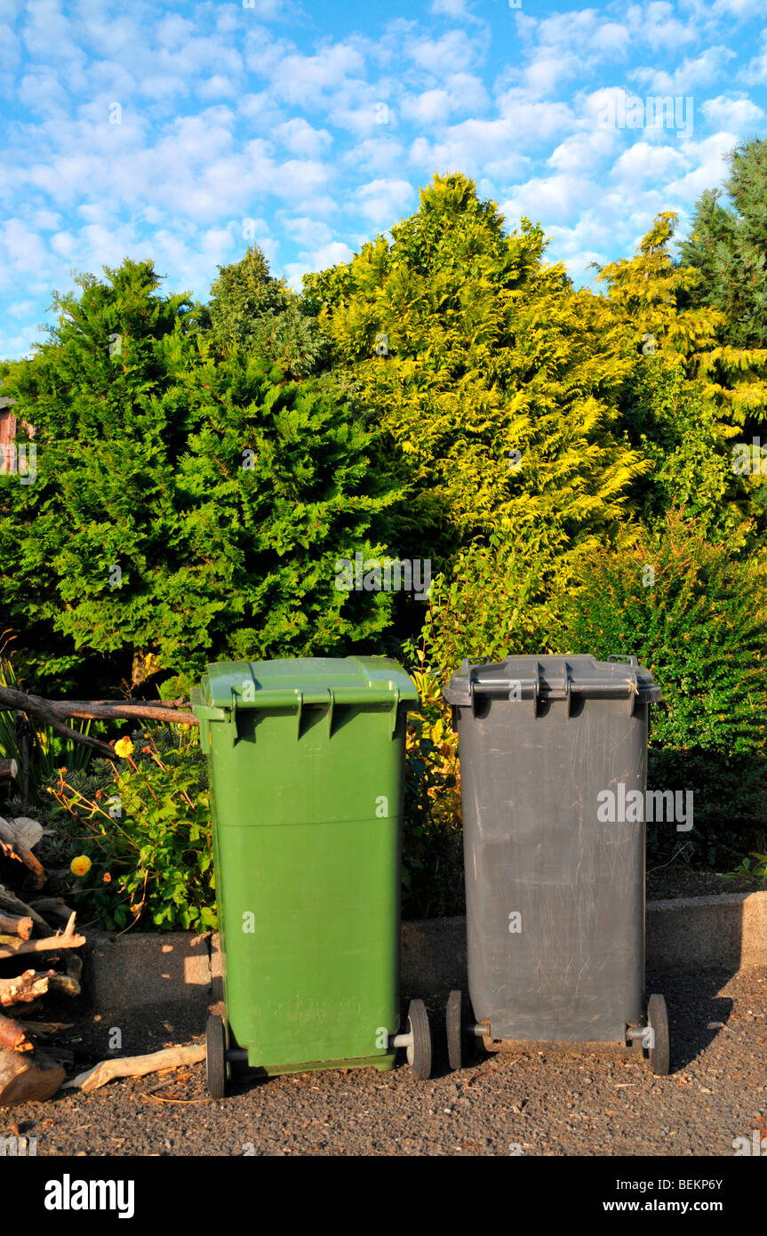 A green and black / grey  wheelie bin sit side by side on the driveway  of a house. Stock Photo