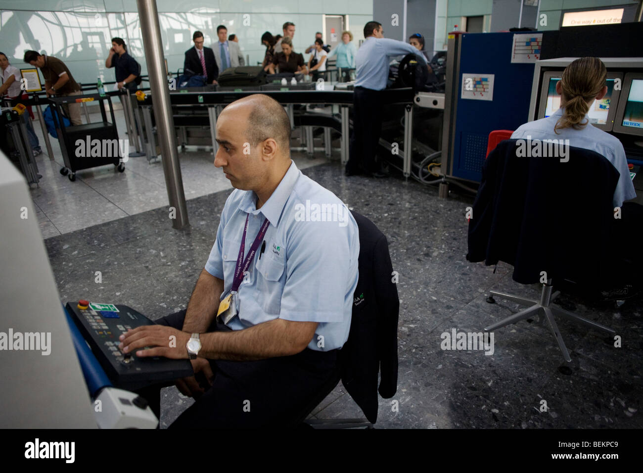 BAA security employed by contractor OCS monitors an X-ray machine at Heathrow Airport's Terminal 5. Stock Photo
