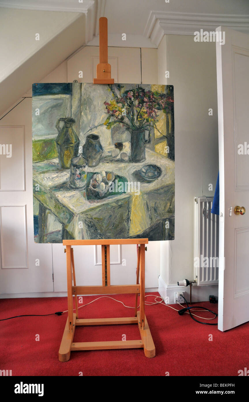 A canvas of a completed  still life painting sits on a wooden easel in a room. Stock Photo