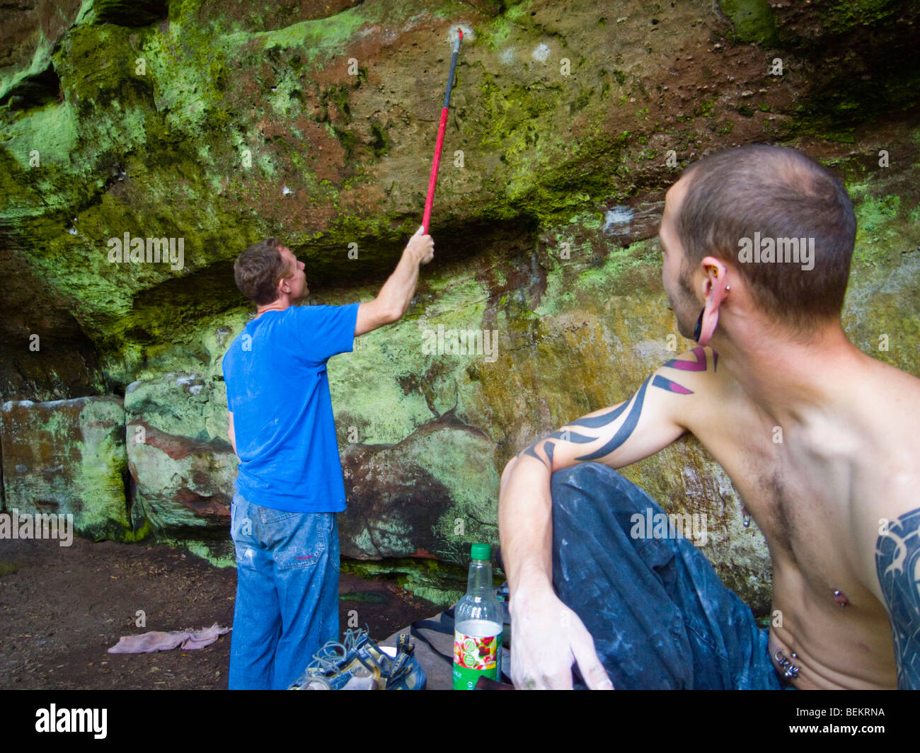 Climber cleaning a hold on a boulder problem, before trying it, whilst his friend watches Stock Photo