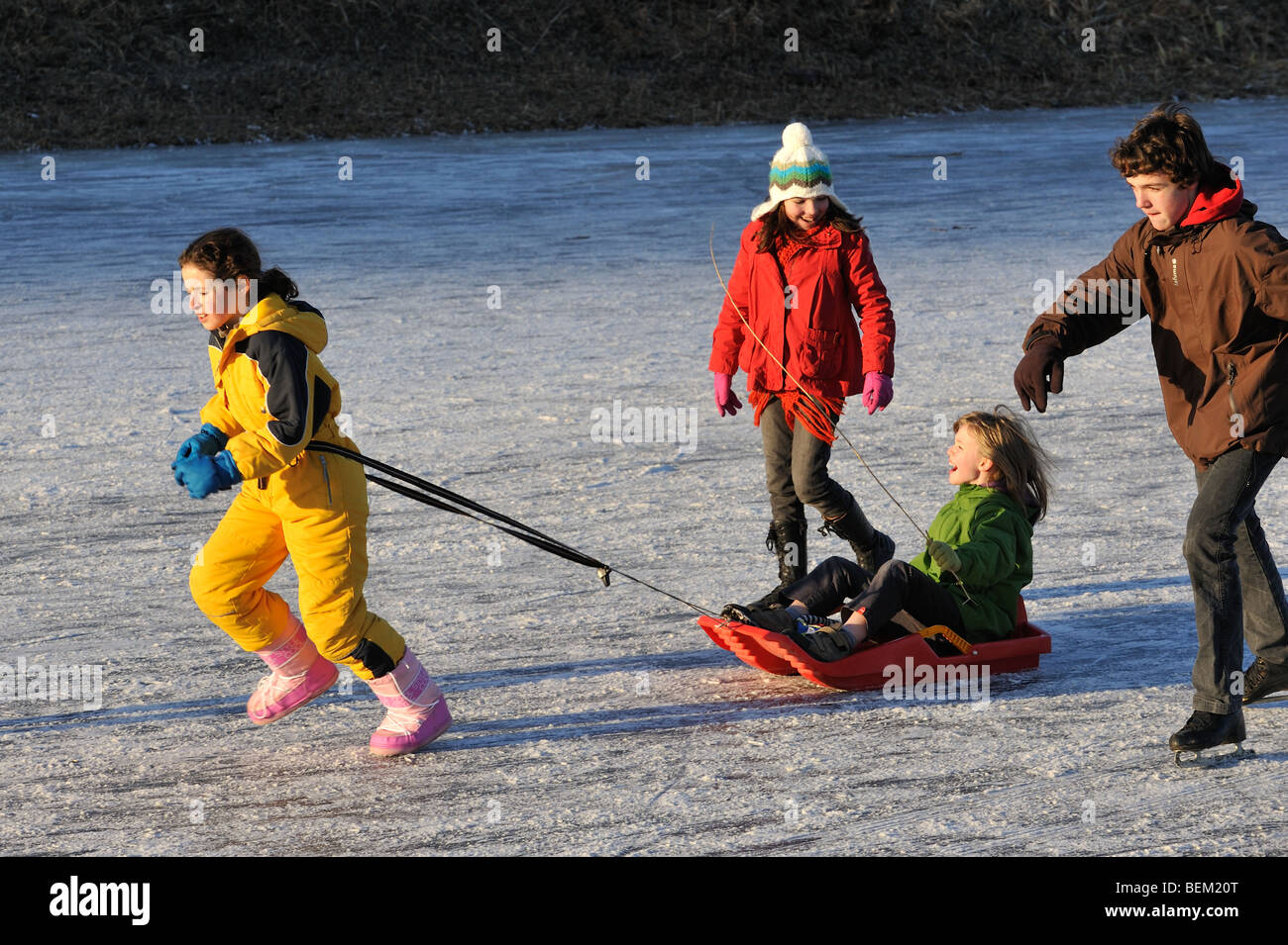 Child on sledge and ice skaters on frozen canal in winter Stock Photo