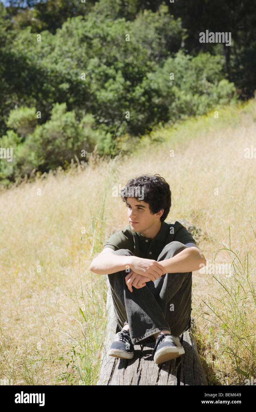 Young male sitting on log Stock Photo