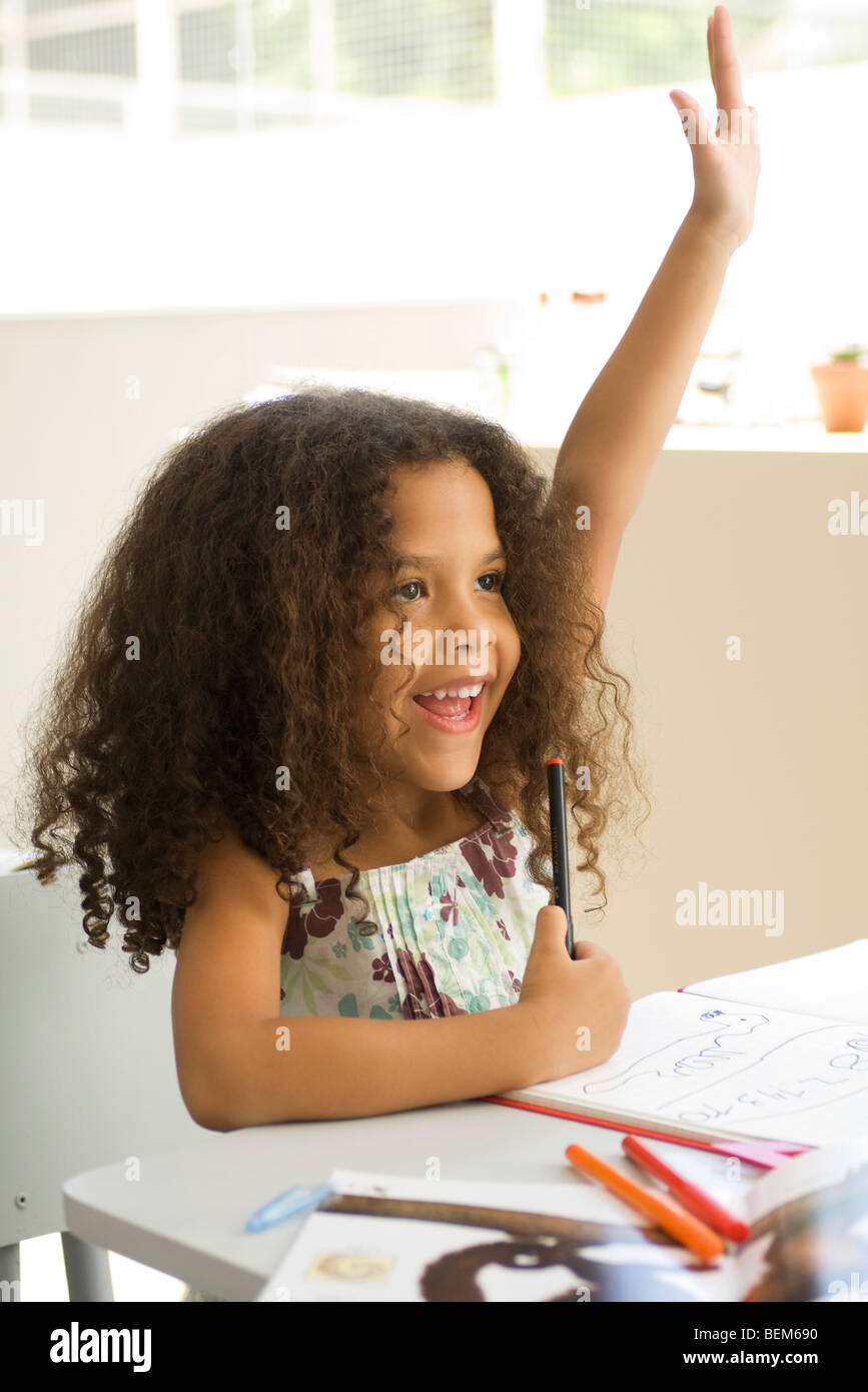 Little girl sitting at school desk, raising hand enthusiastically Stock ...