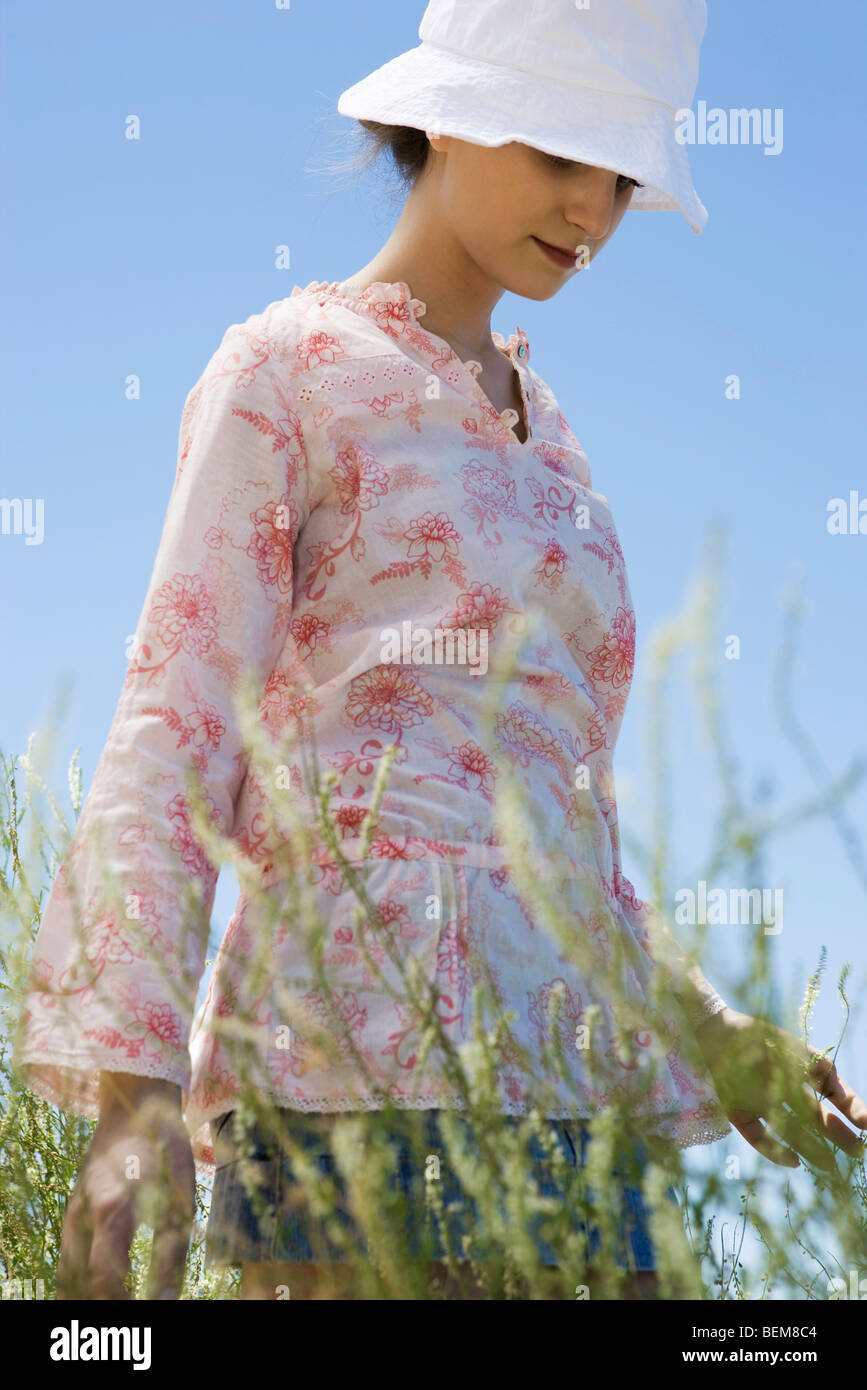 Young woman wearing sunhat, walking through tall grass Stock Photo