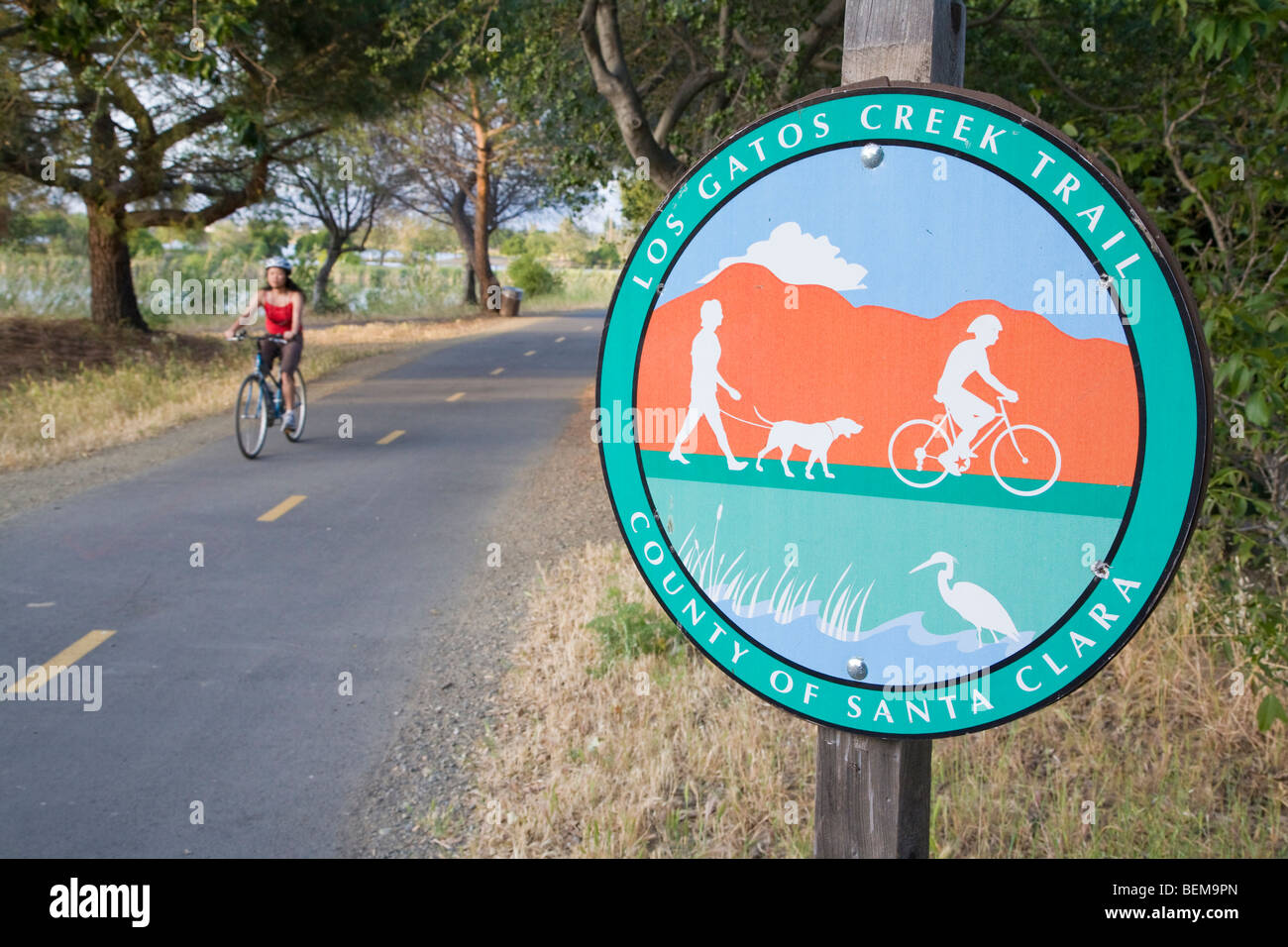 Sign of Los Gatos Creek Trail, multi-use trail, in Santa Clara County. A female cyclist in the background. Stock Photo