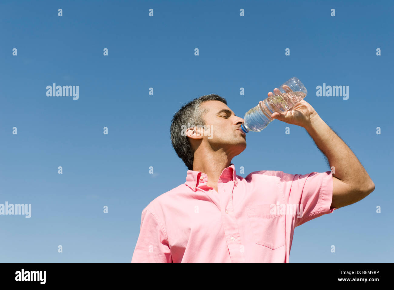 Man standing outdoors drinking from bottle of water, low angle view, blue sky in background Stock Photo