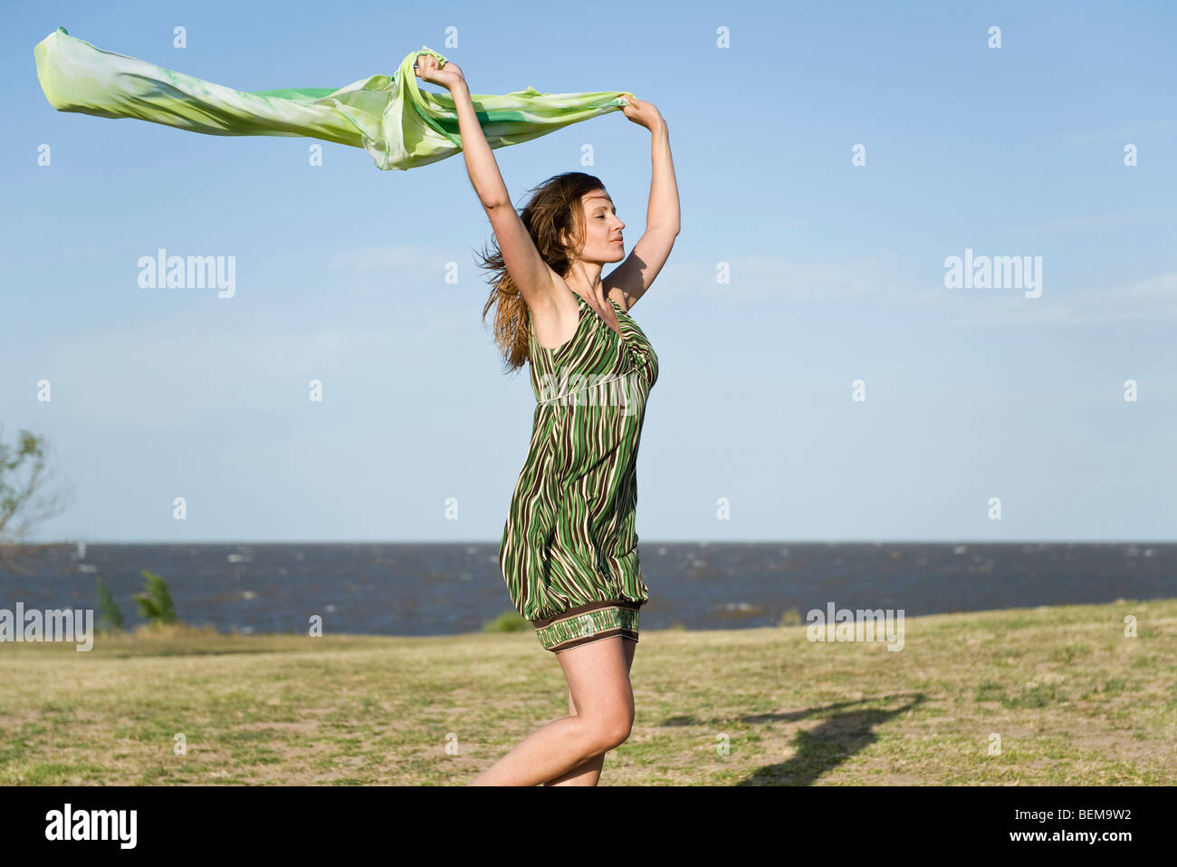 Woman walking in wind, holding up shawl in the air, full length Stock Photo
