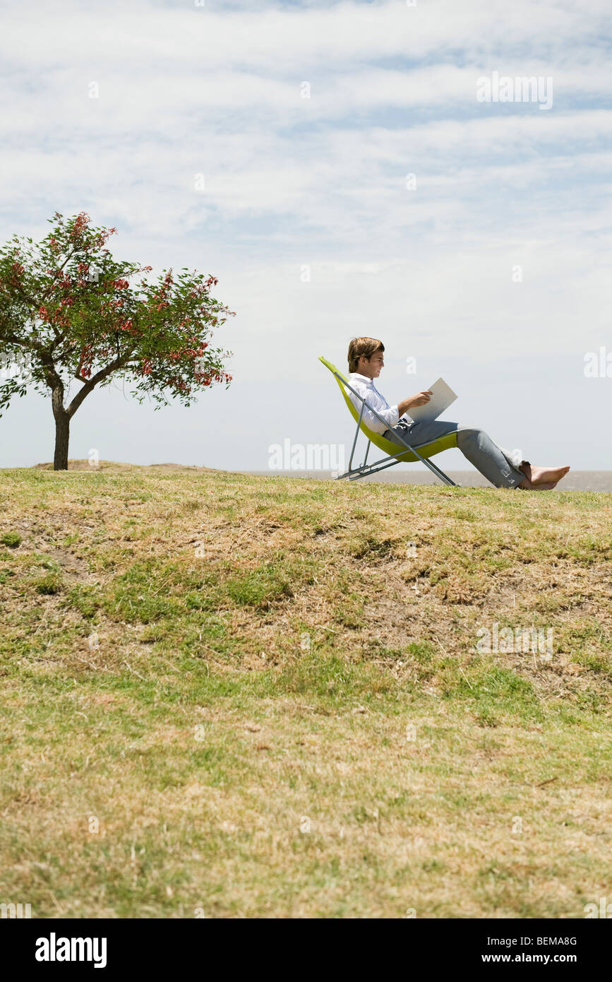 Man relaxing outdoors reading through binder Stock Photo
