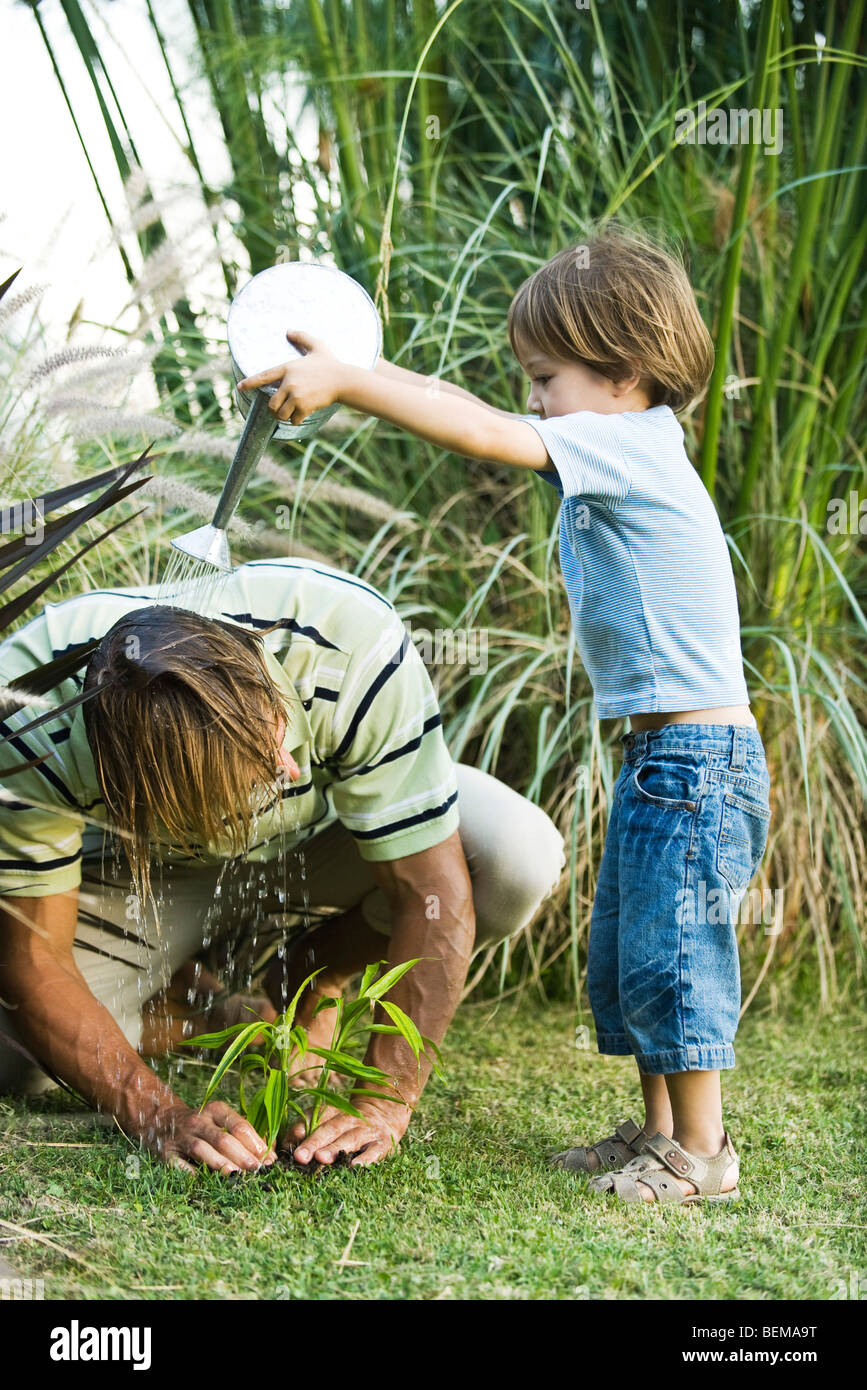 Little boy pouring water on his father's head as he works in garden