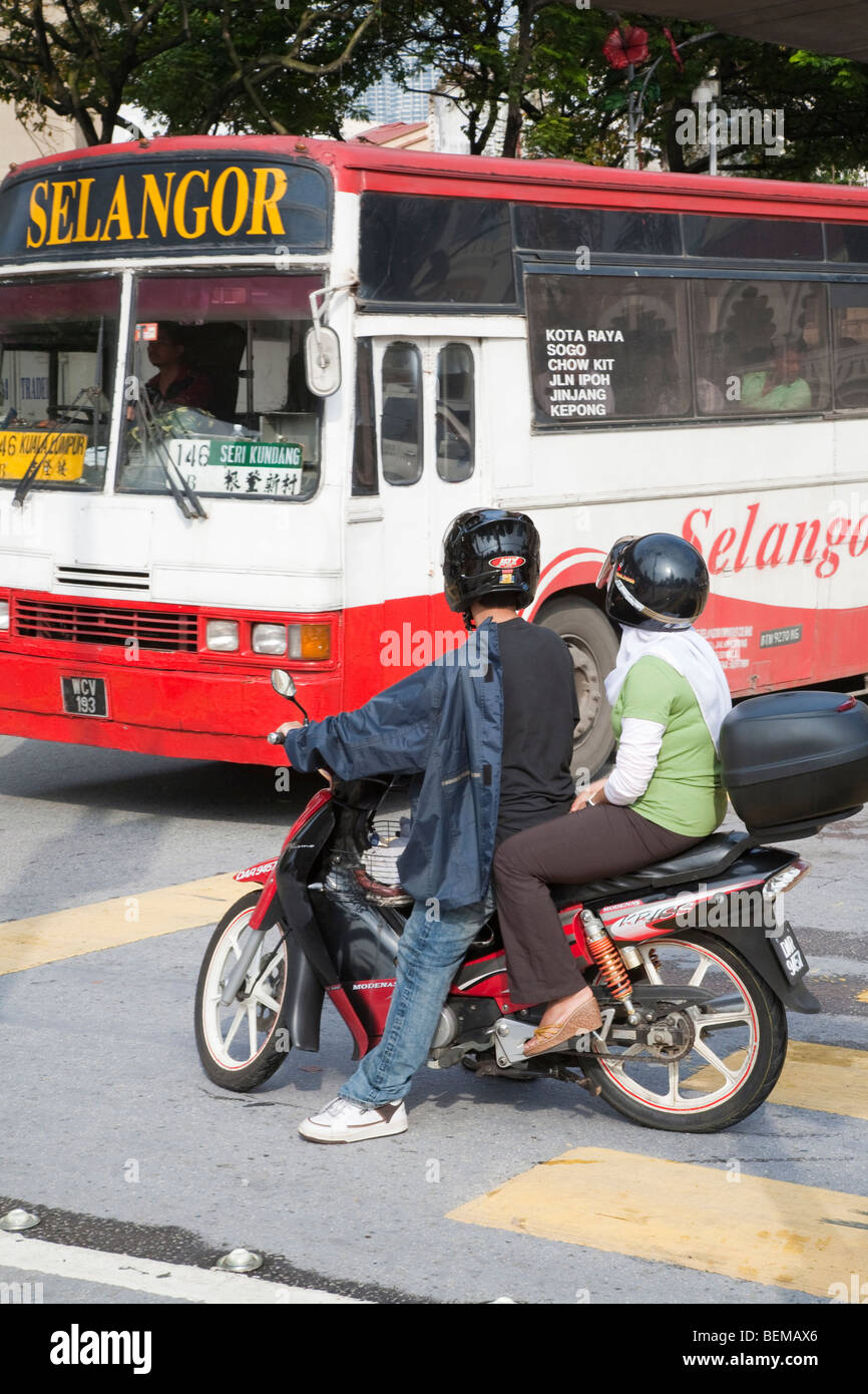 Two people on a moped giving way to a city bus in downtown Kuala Lumpur. Kuala Lumpur, Selangor, Malaysia Stock Photo