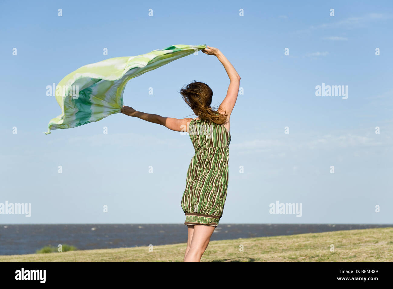Woman standing outdoors, holding up shawl in wind, full length Stock Photo