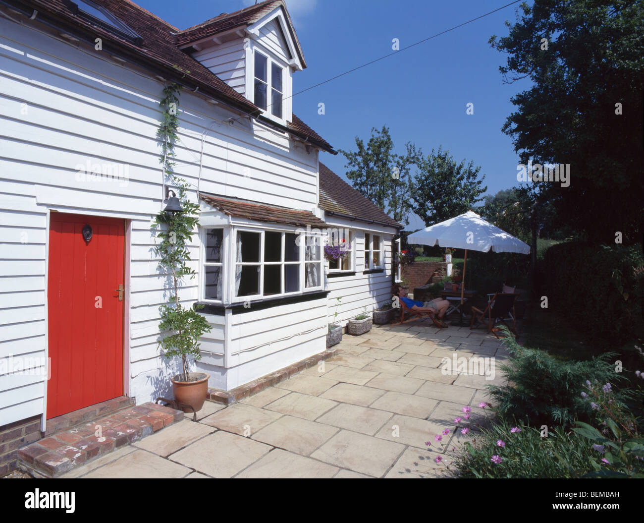 White clapboard house with red door and small paved patio Stock Photo