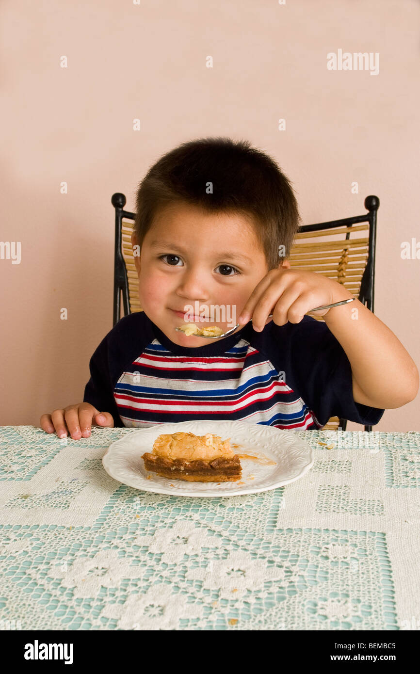 first bite3-4 year old Hispanic boy eating Apple pie at table  eye contact  California MR Myrleen Pearson Stock Photo