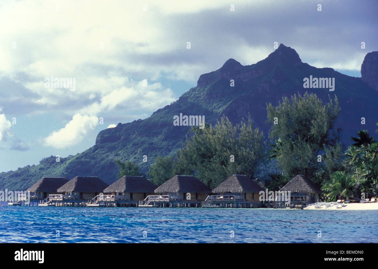 Small water bungalows at coast, in South Pacific. Bora Bora in background. French Polynesia. Stock Photo