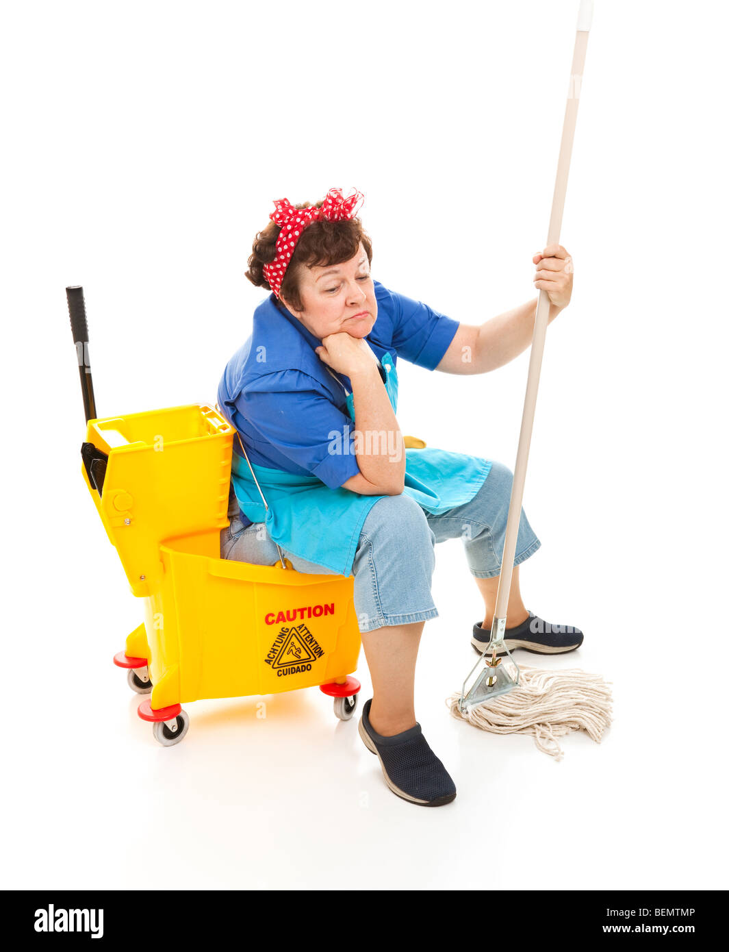 Depressed maid sitting in her bucket and holding her mop, with a sad expression on her face. Full body isolated. Stock Photo