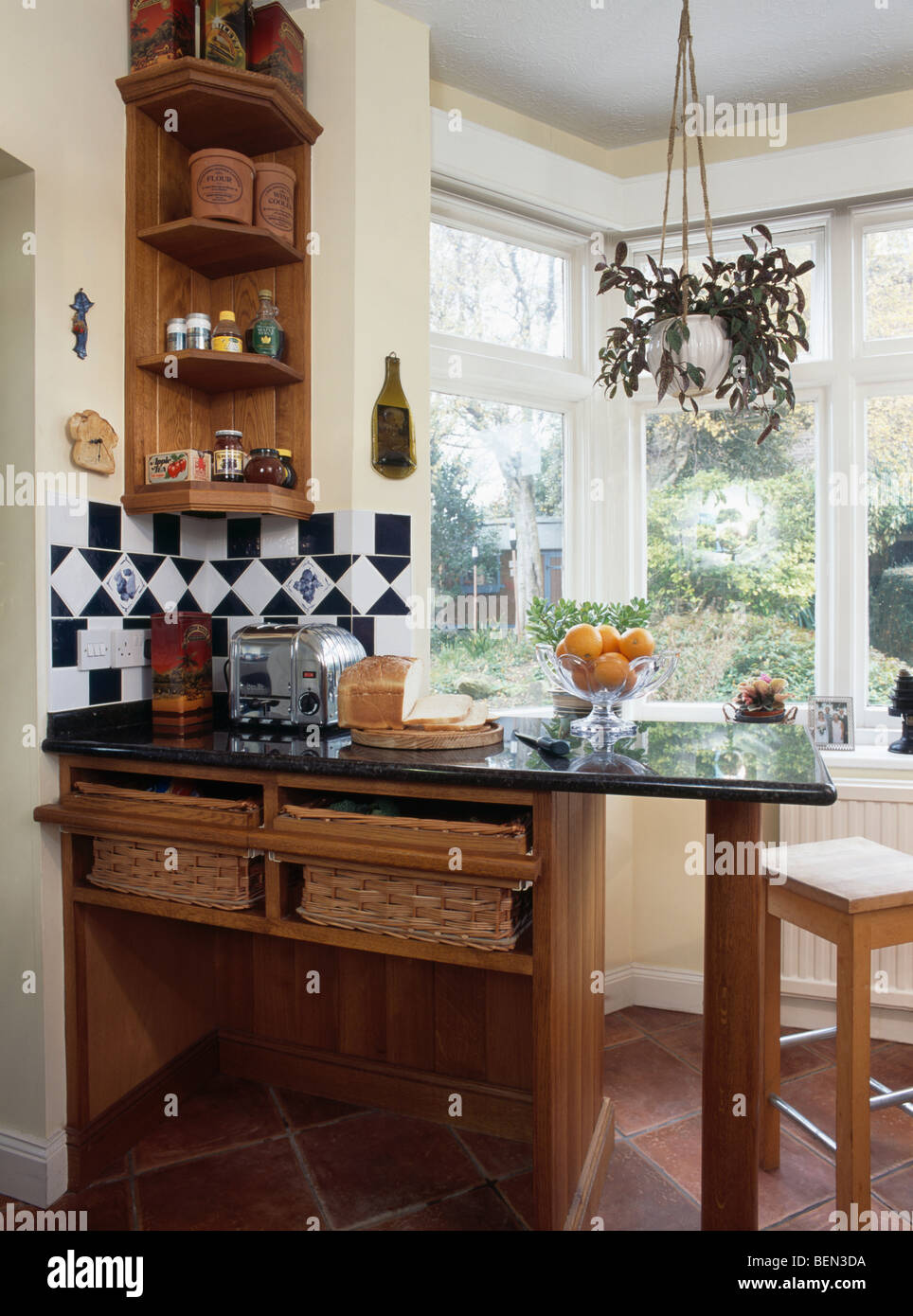 Small wood shelf unit above granite-topped breakfast bar with storage baskets below worktop in country kitchen Stock Photo