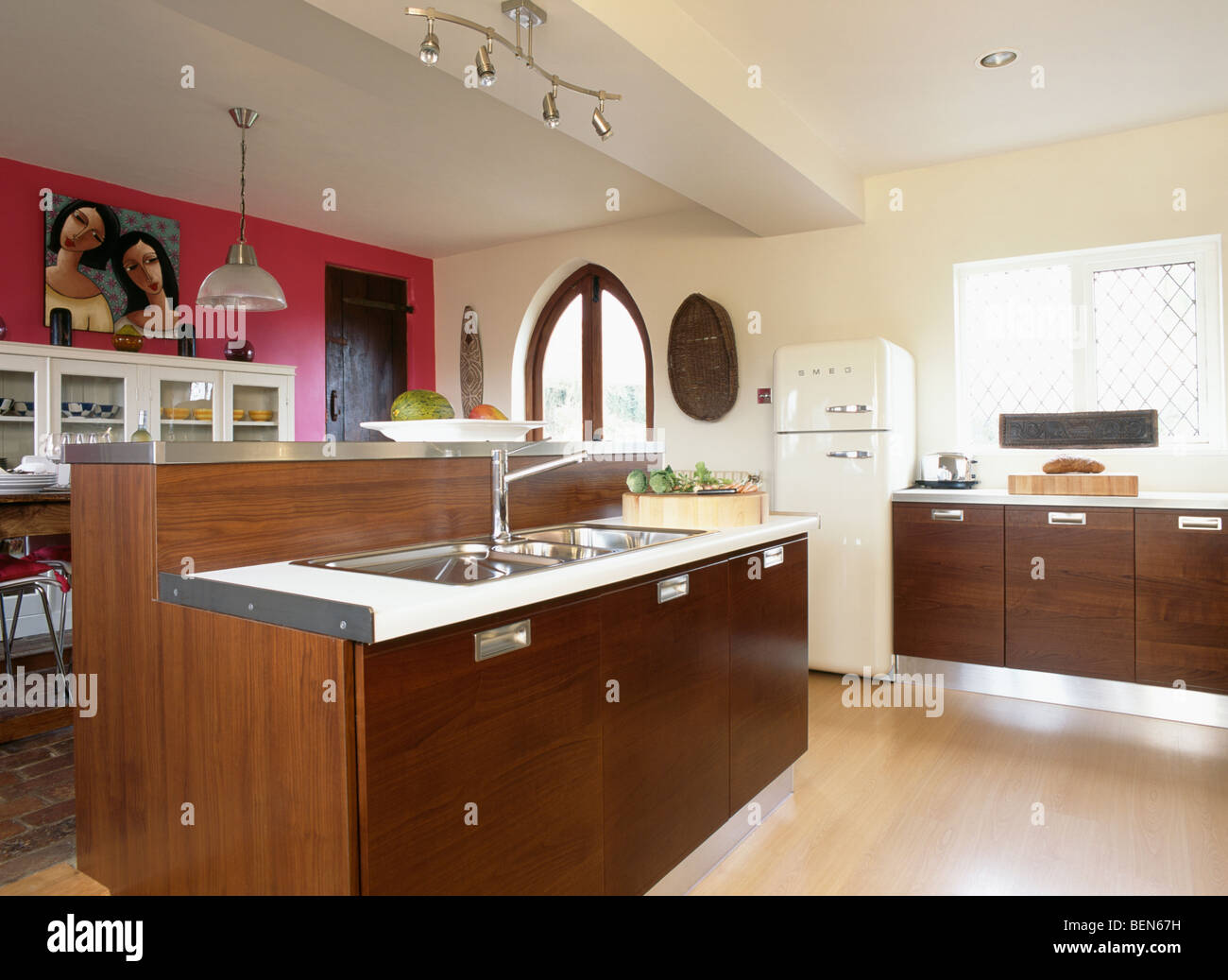 Pink wall in large modern cream kitchen with dark wood units and double stainless-steel sinks in island unit Stock Photo