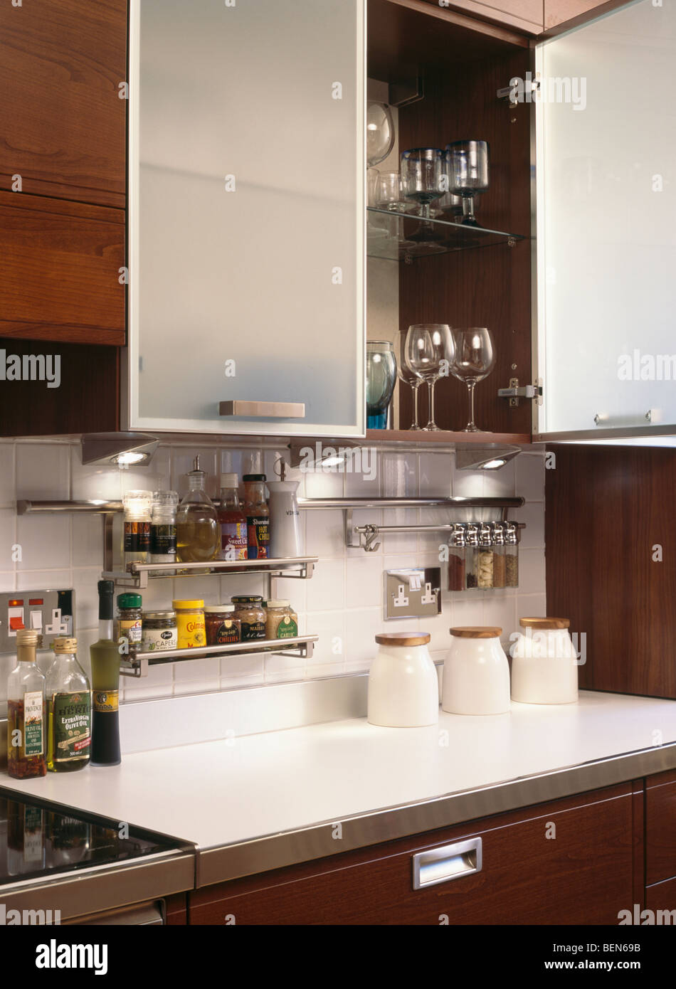 Close-up of kitchen cupboard with opaque glazed doors open above small storage shelves and white worktop Stock Photo