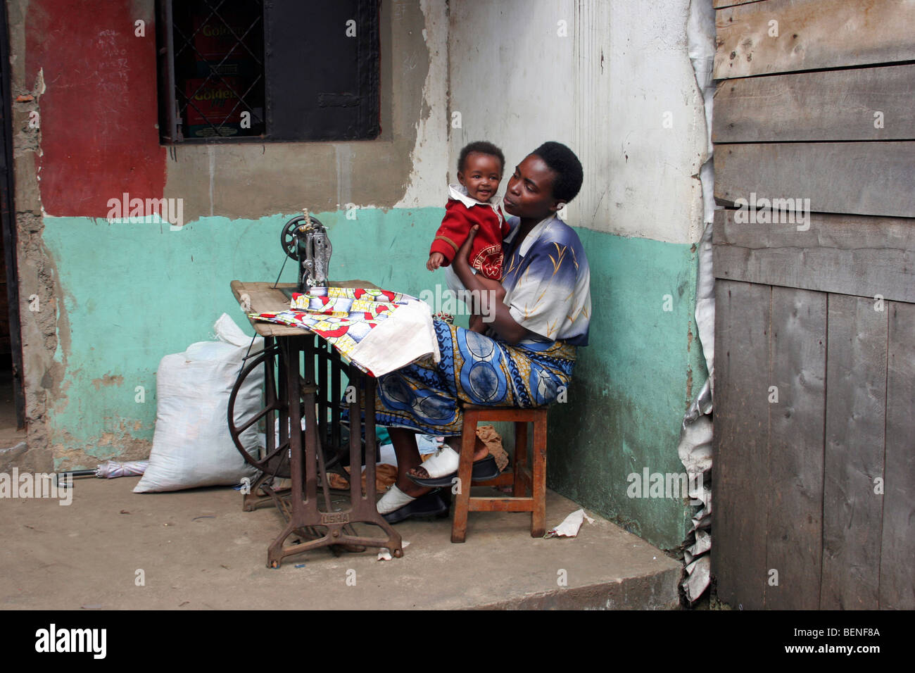 Seamstress with child working with old Usha treadle sewing machine at home, Ruhengeri, Musanze, Rwanda, Central Africa Stock Photo