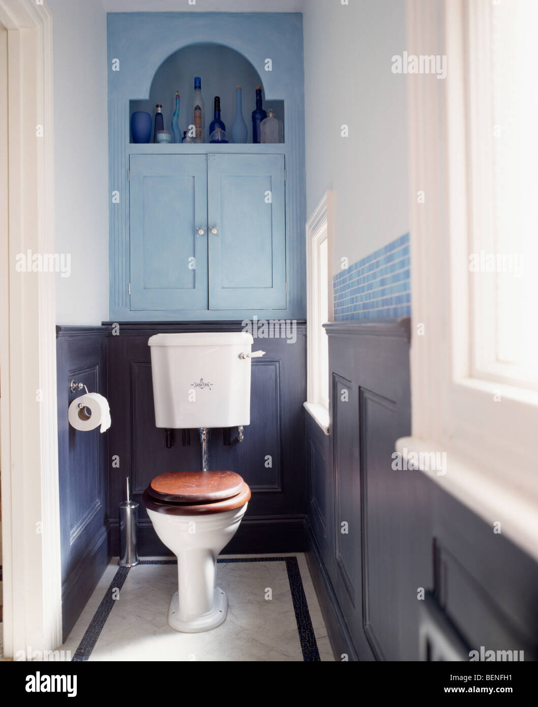 Pale blue fitted cupboard above toilet with mahogany seat in small