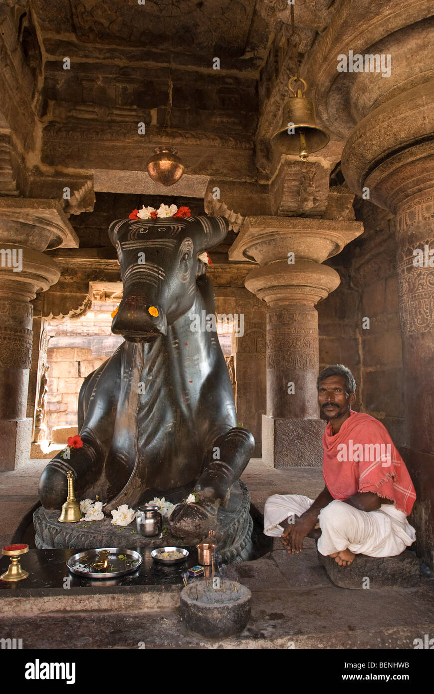 Man sitting next to a Monolith Nandi Statue in Nandi Mandapa Pattadakal Karnataka India Stock Photo
