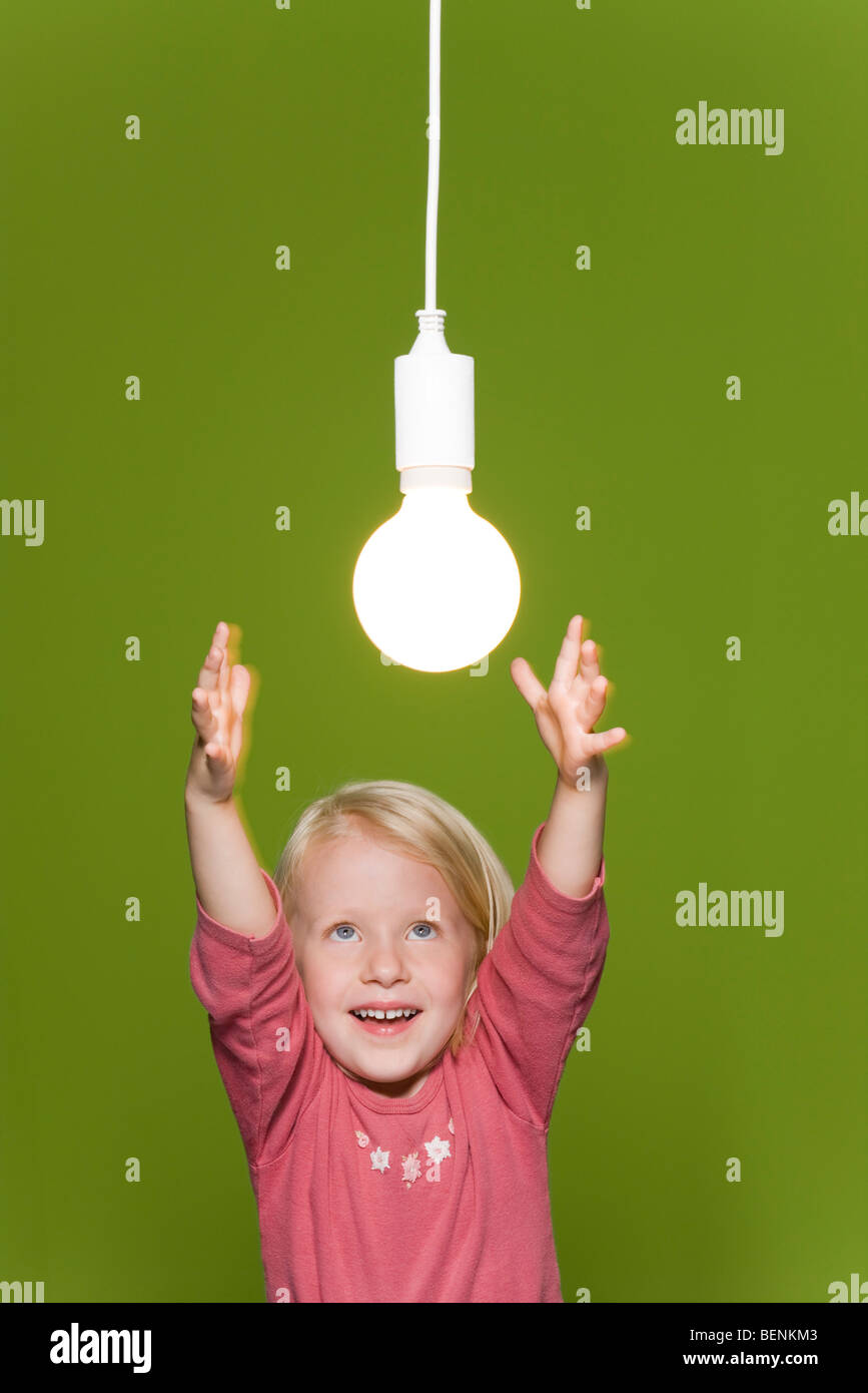 Little girl reaching for hanging light bulb Stock Photo