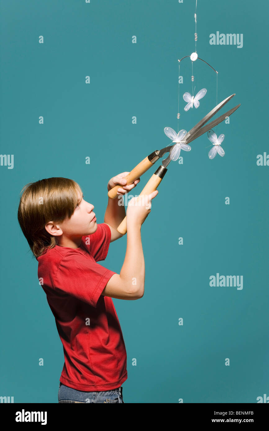 Boy using hedge clippers to cut down butterfly mobile Stock Photo