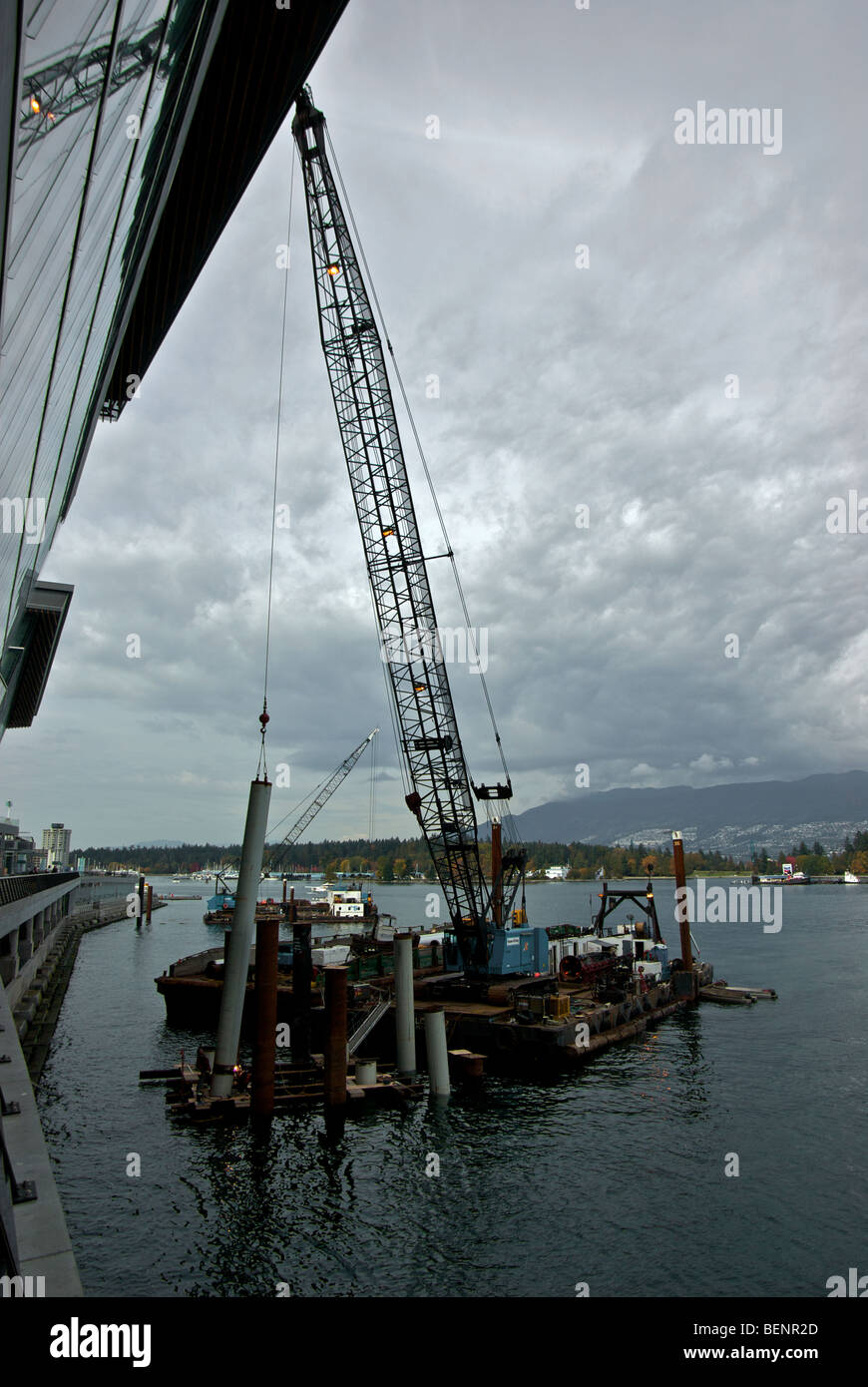 Welders working on steel piling held in place with enormous crane on barge at Vanouver Trade and convention Centre addition Stock Photo
