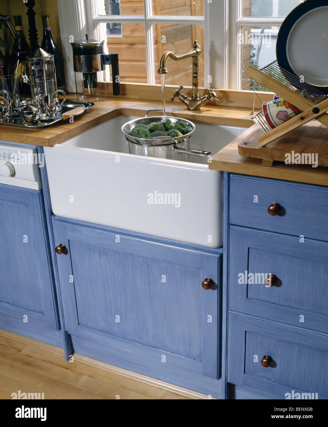 Close-up of Belfast sink below window in kitchen with fitted blue units Stock Photo