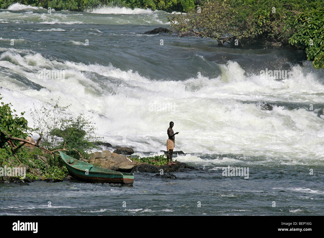 Black man on riverbank fishing in the rapids of the river White Nile