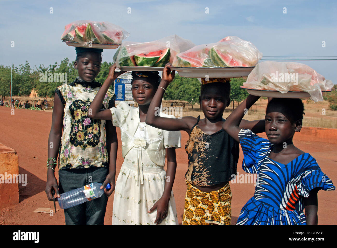 Black children carrying fruit on their heads along dirt road, Sahel, Mali, West Africa Stock Photo
