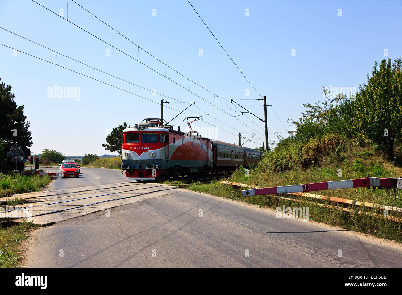 Train (pulled by an electric ASEA / Rade Koncar) locomotive and cars at a railroad crossing in Transylvania, Romania Stock Photo