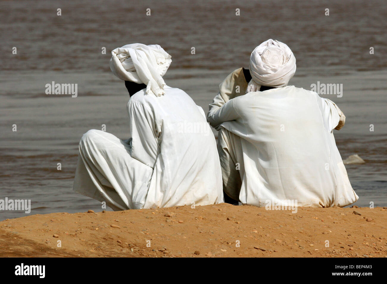 Two Nubian men dressed in white thawbs / thobes / dishdashas sitting on riverbank of the river Nile, Sudan, North Africa Stock Photo