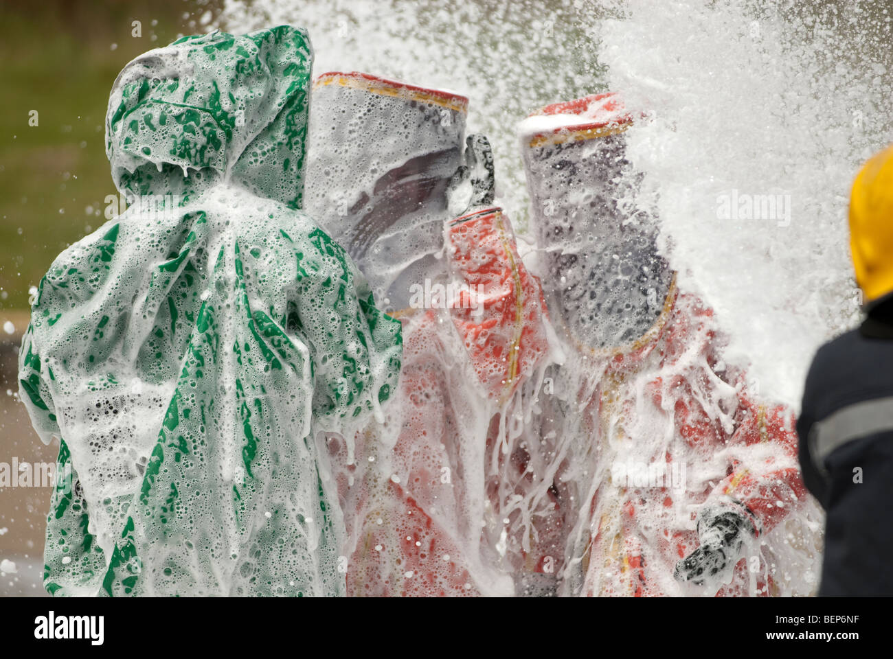 firefighters in gas tight suits being doused with foam Stock Photo