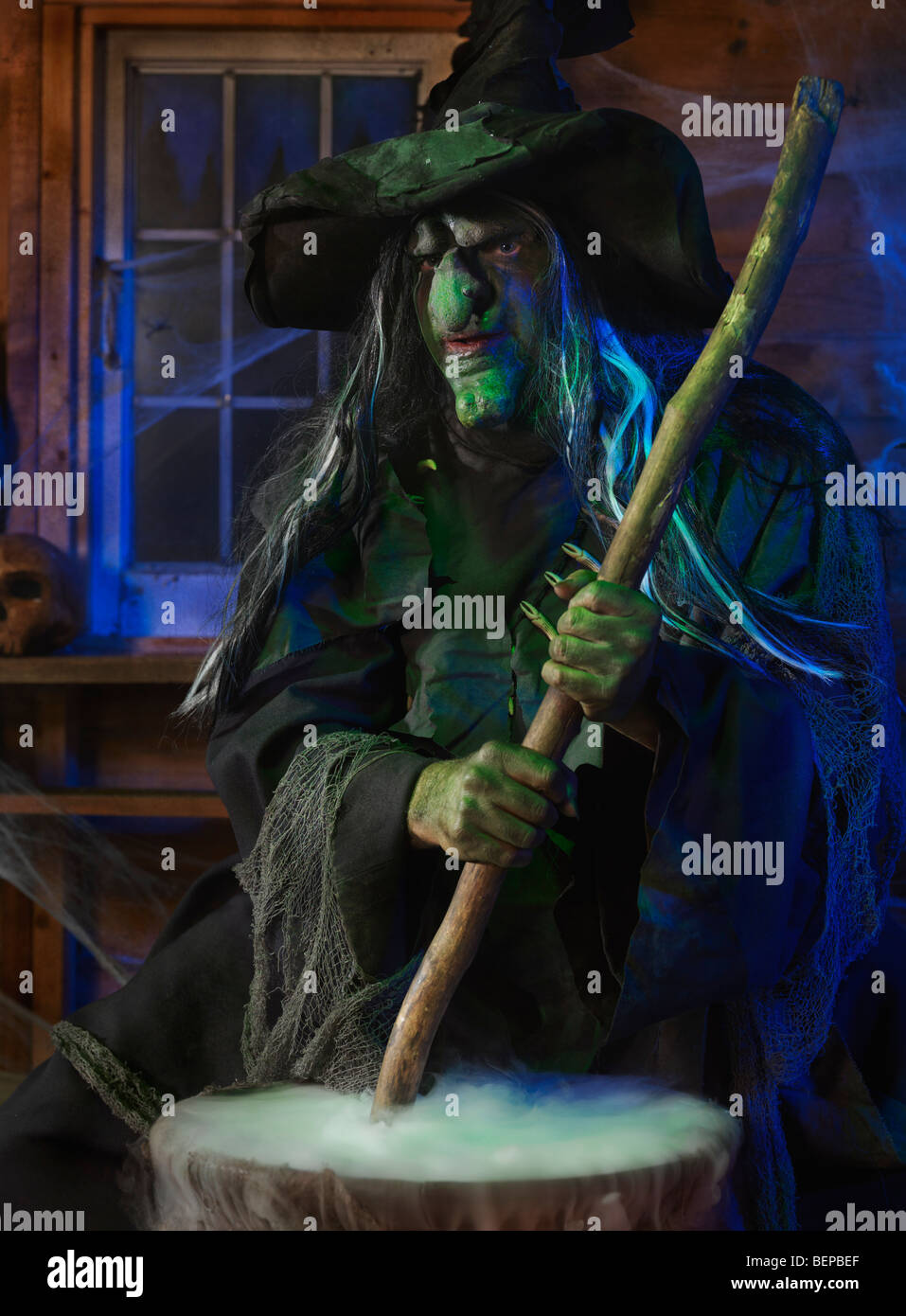 Scary old witch stirring potion in a cauldron inside her cabin on