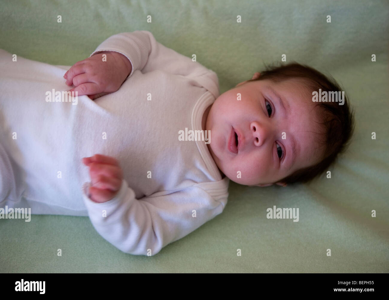 Baby lying down wearing white grower pulling funny face Stock Photo Alamy